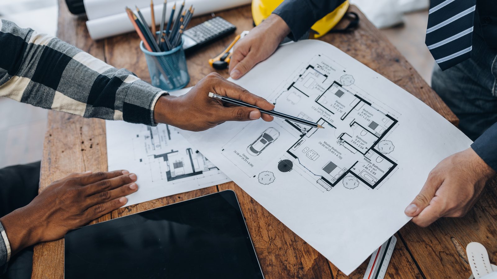 Plan de plancher détaillé désigné au crayon, entouré d'autres feuilles de plans de construction sur une table de bois.